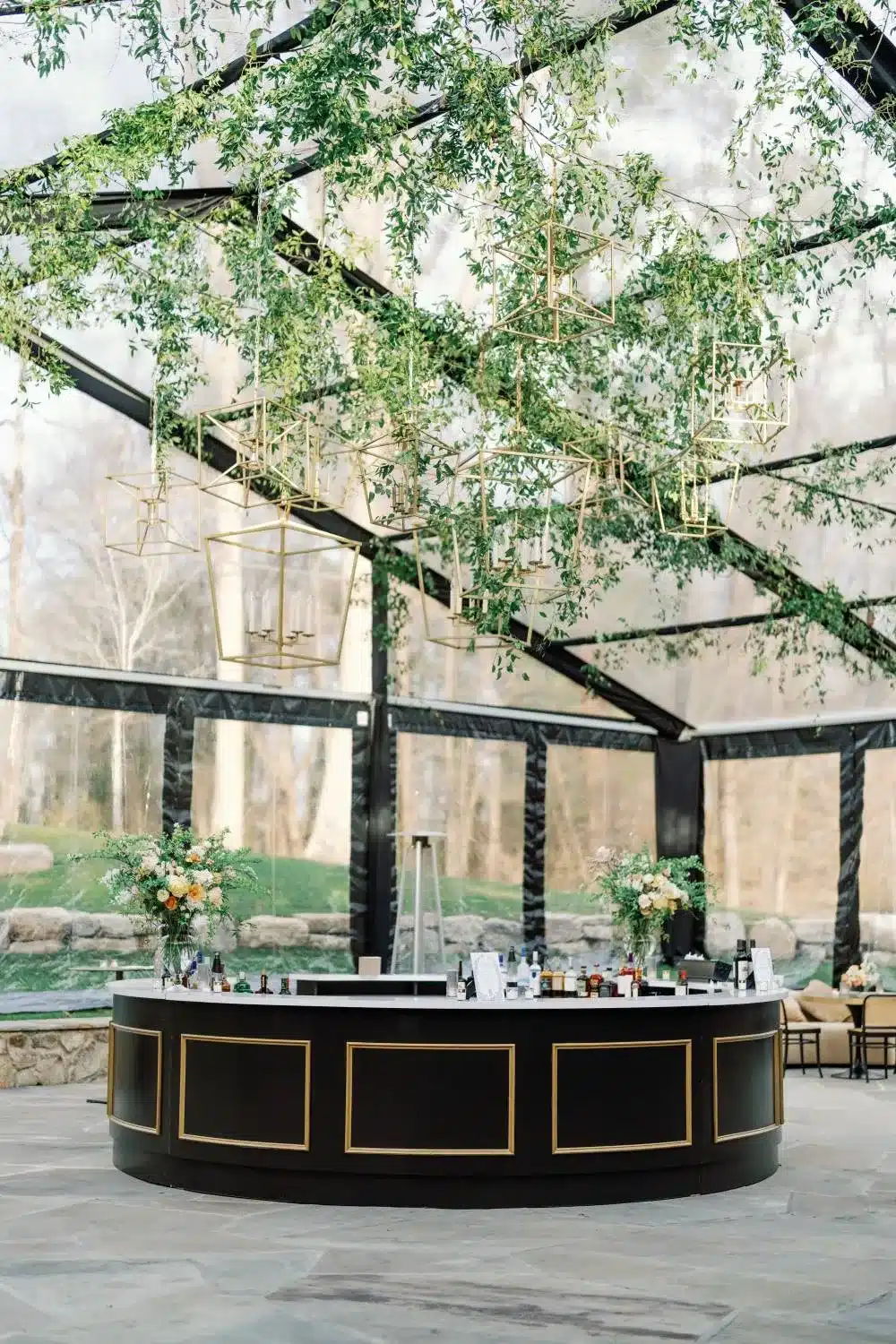 Round black bar with gold accents under greenery and modern lantern lighting in a clear tent