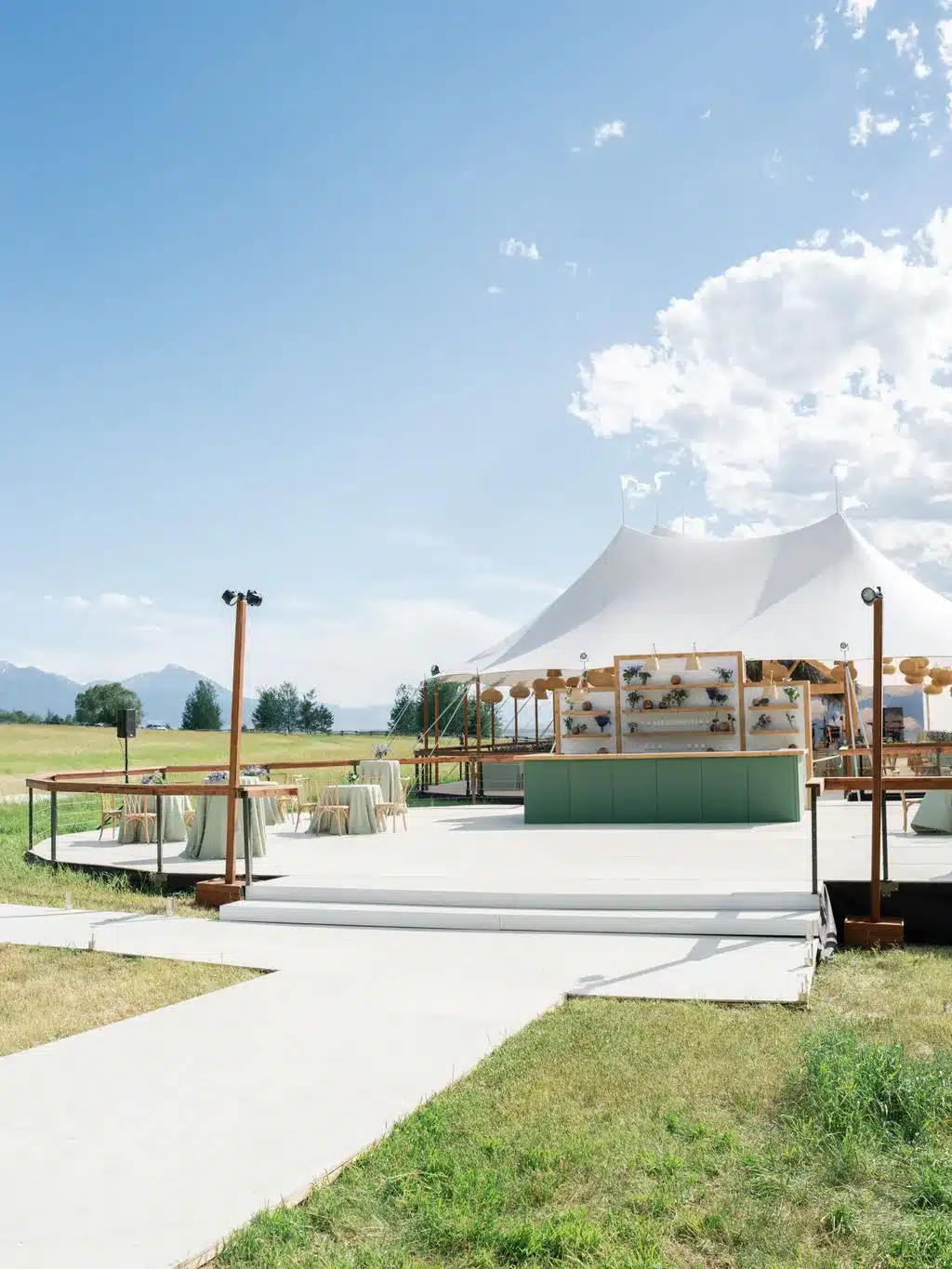 An outdoor event setup with a custom bar and a sailcloth tent on open grounds.