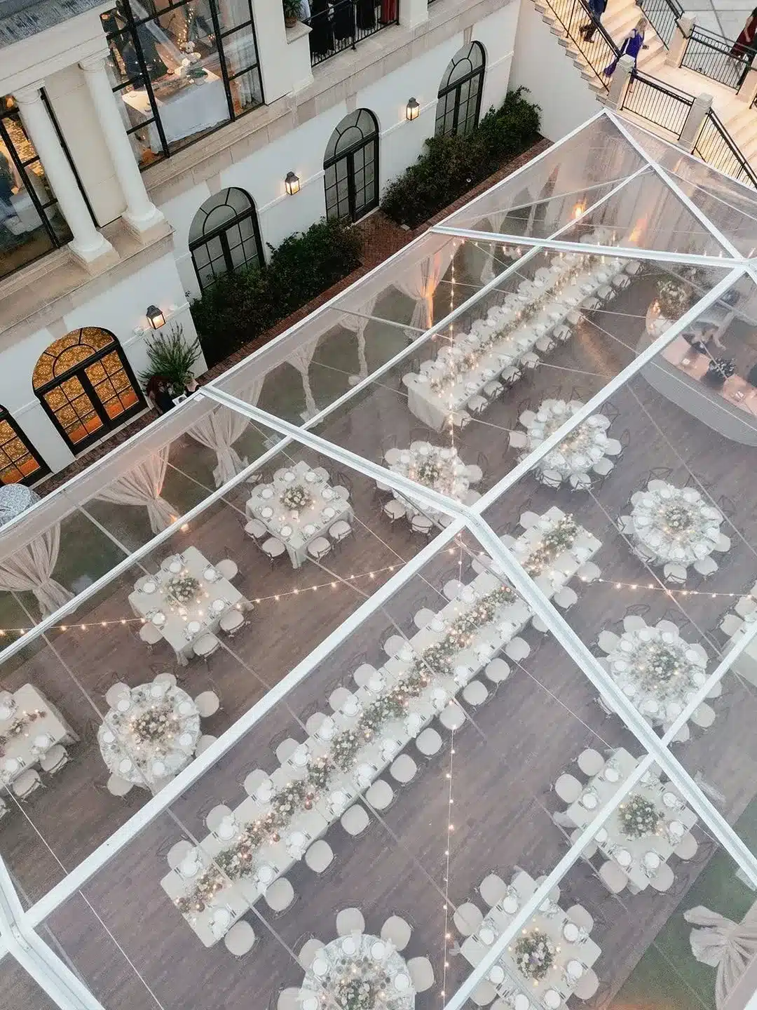 A clear-top tent set for an elegant dinner with long banquet tables and soft lighting.