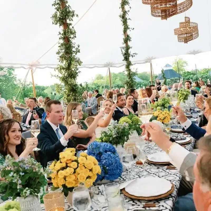 Guests raising glasses inside a festive tent decorated with greenery and vibrant floral centerpieces.