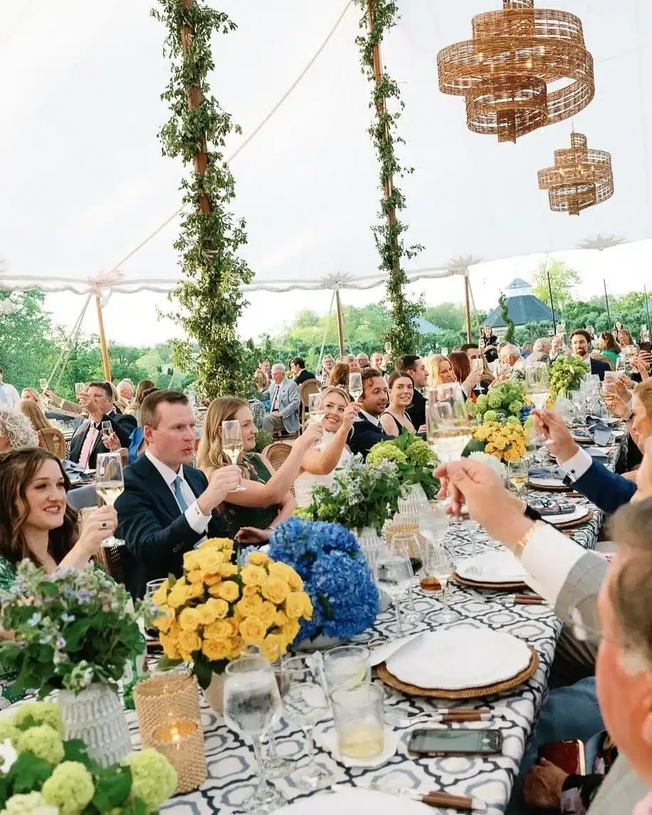 Guests raising glasses inside a festive tent decorated with greenery and vibrant floral centerpieces.