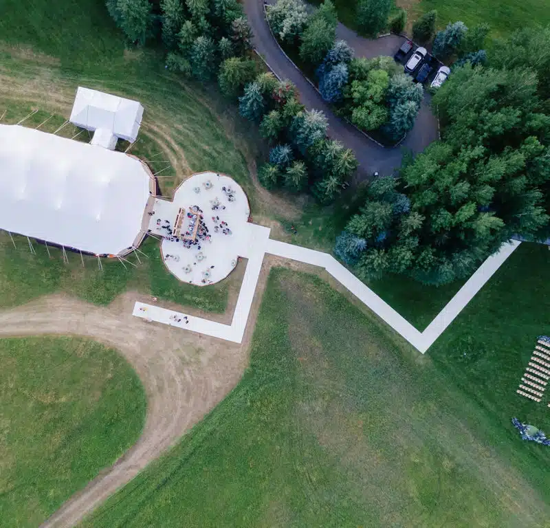 Aerial view of an elegant white event tent beside a round patio surrounded by trees.