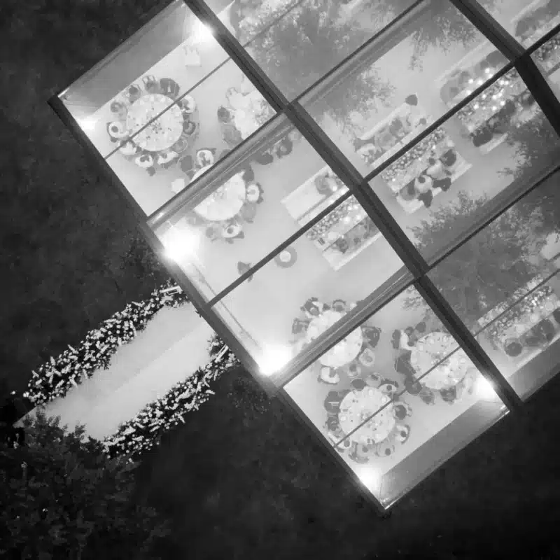 Black-and-white aerial view of a clear-top tent reception with glowing perimeter lights.