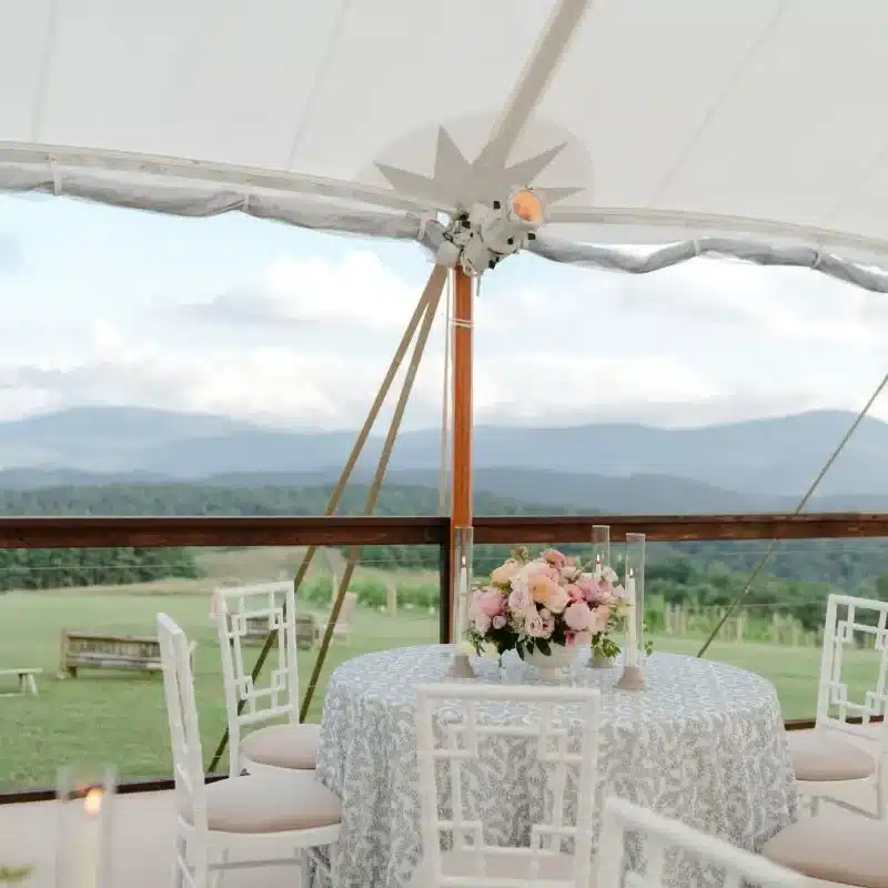 Round table with patterned linen and pastel florals inside a tent overlooking mountain views.