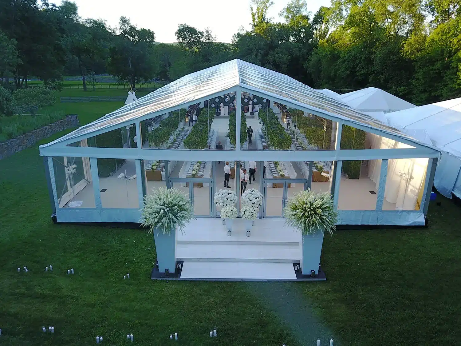 Clear-top tent entrance with white steps and large floral arrangements on pedestals.