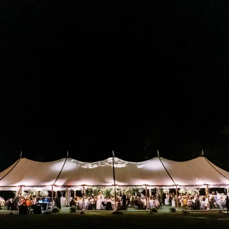 Nighttime sailcloth wedding tent glowing with string lights and seated guests