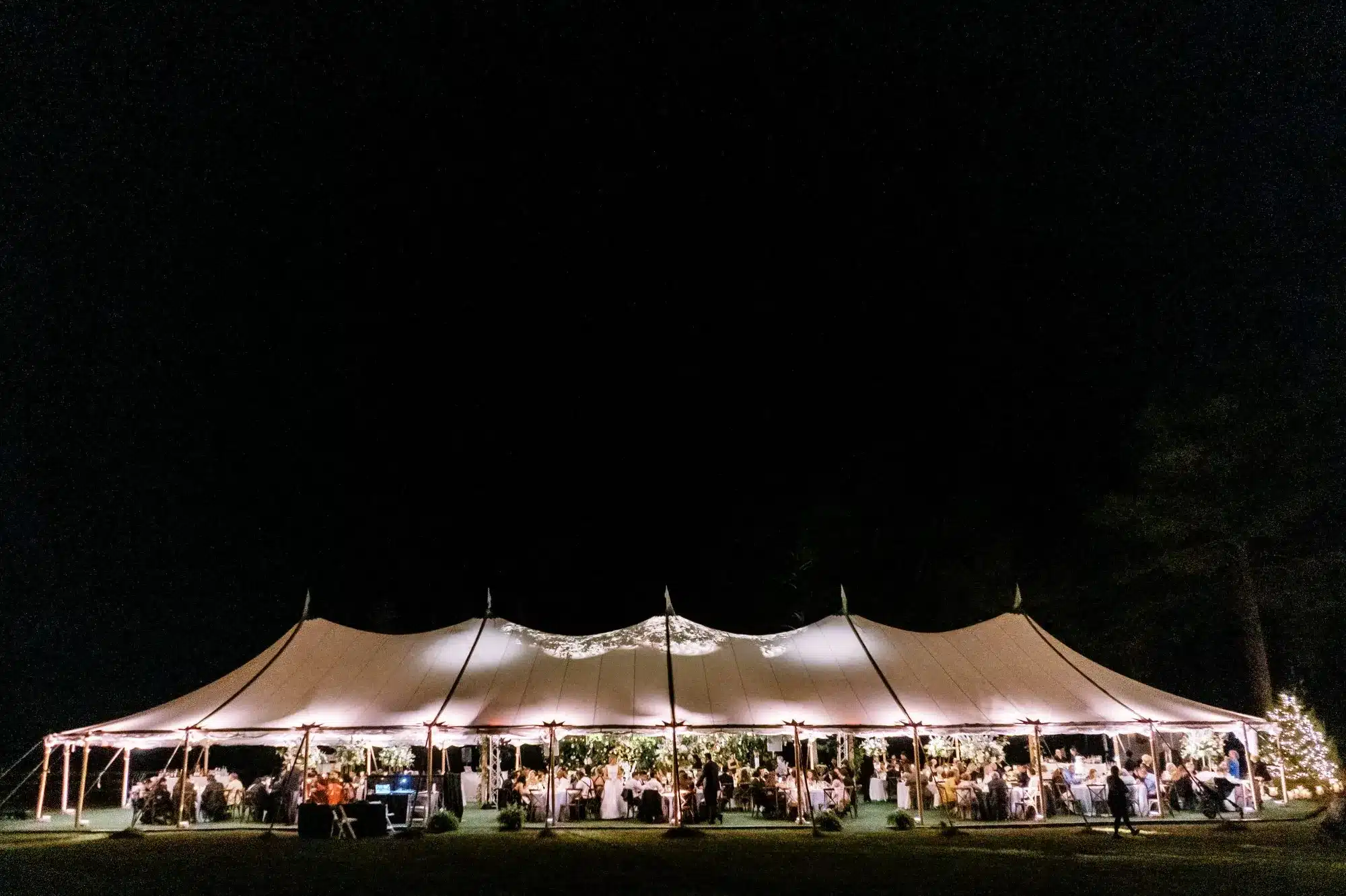 Nighttime sailcloth wedding tent glowing with string lights and seated guests