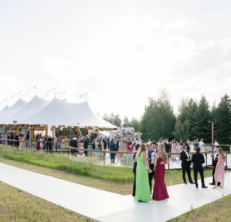 Guests walk toward a large outdoor event tent set up on a grassy property