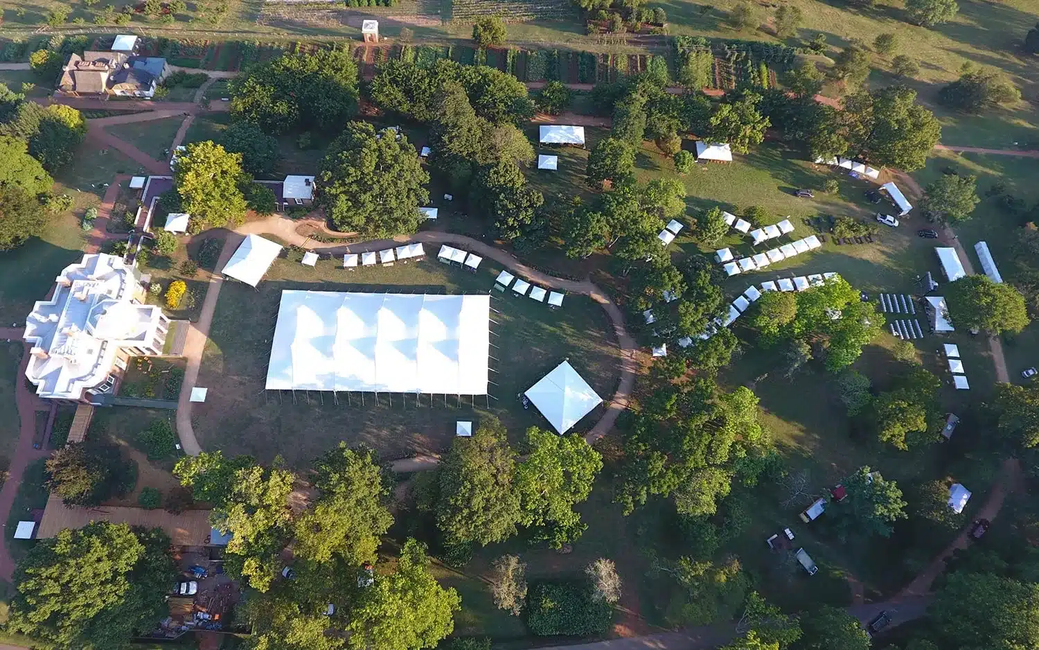 Aerial view of a large white backyard event tent rental set among trees and landscaped grounds.