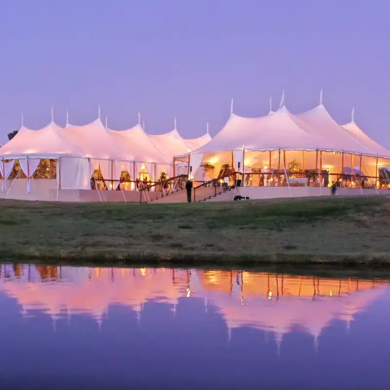 Elegant event tent setup by water, showcasing illuminated interior and stylish decor, ideal for outdoor gatherings and weddings, reflecting Skyline Tent Company's event planning expertise.