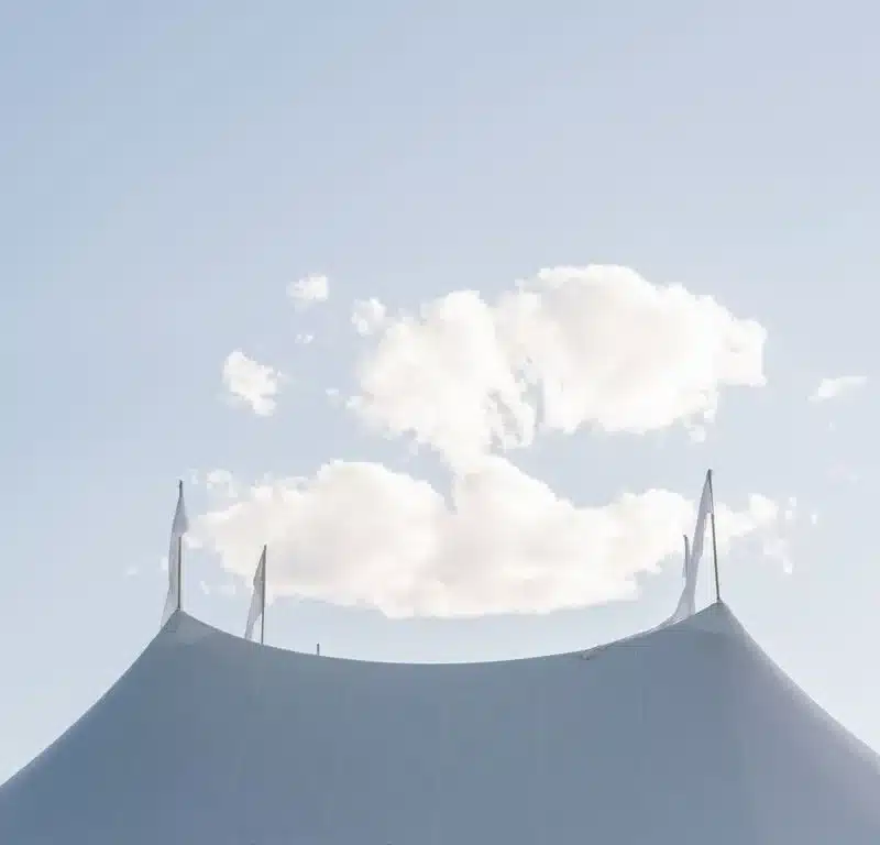 Large white tent with pointed peaks under a clear sky and fluffy clouds, symbolizing outdoor event elegance and luxury tent rentals.
