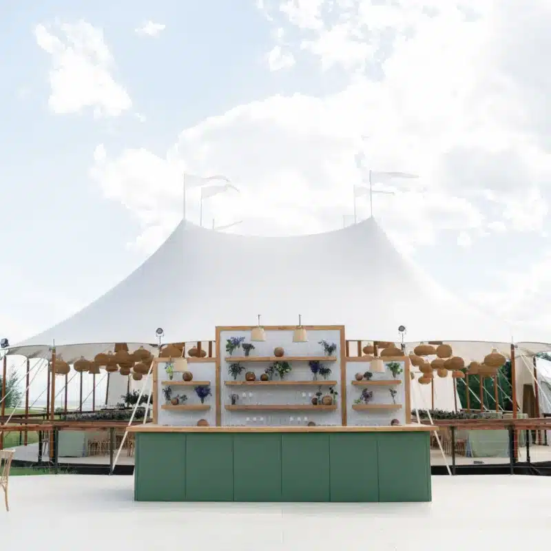 Elegant outdoor tent with a stylish bar setup, featuring shelves adorned with decorative items and flowers, enhancing the luxury event atmosphere.