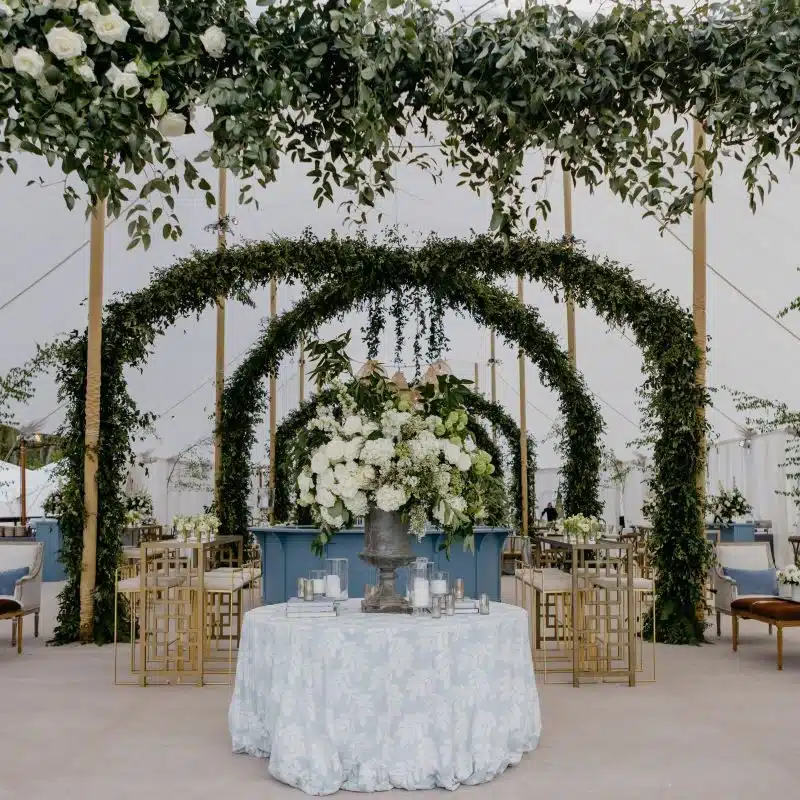 Elegant tent interior featuring lush floral arrangements, greenery arches, and a decorated table, ideal for luxury outdoor events and weddings.
