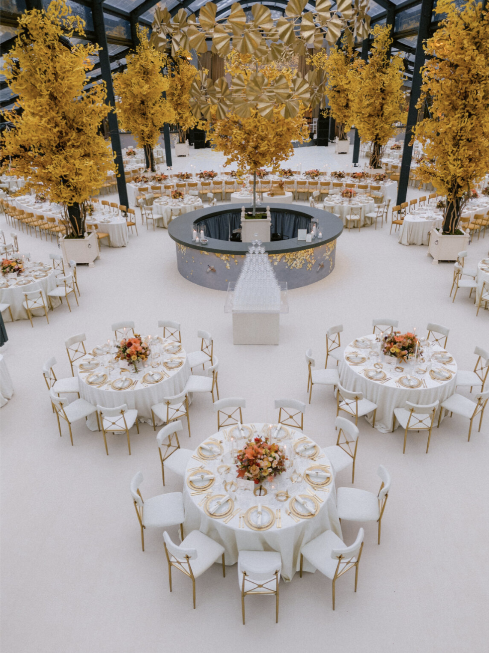 Circular bar surrounded by evenly spaced round dining tables with elegant place settings under a decorated tent.