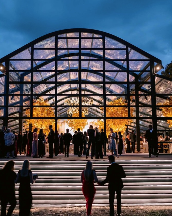 Evening event inside a glass-walled tent with guests mingling under warm lighting.