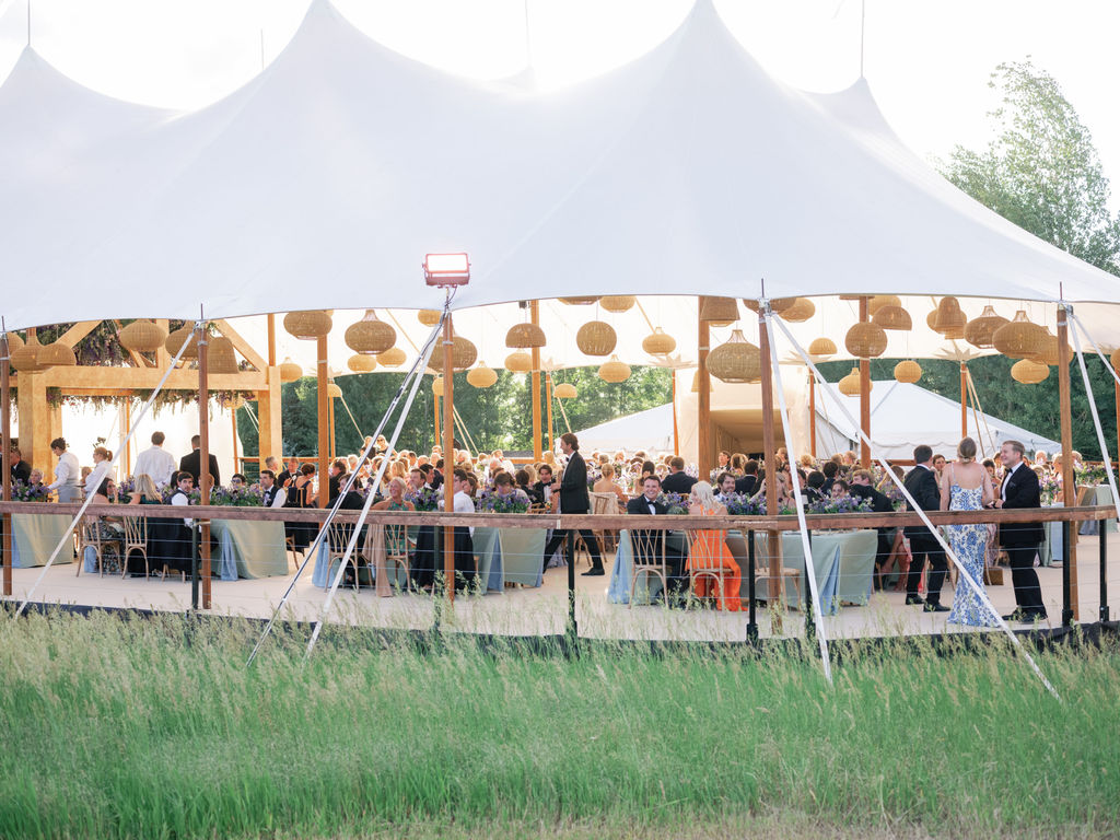 Guests seated at round tables inside a sailcloth tent with woven lanterns overhead.