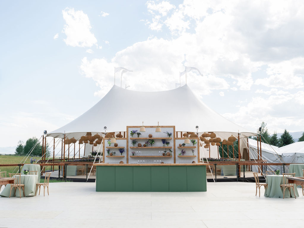 Symmetrical outdoor bar display set in front of a sailcloth tent on an open lawn.