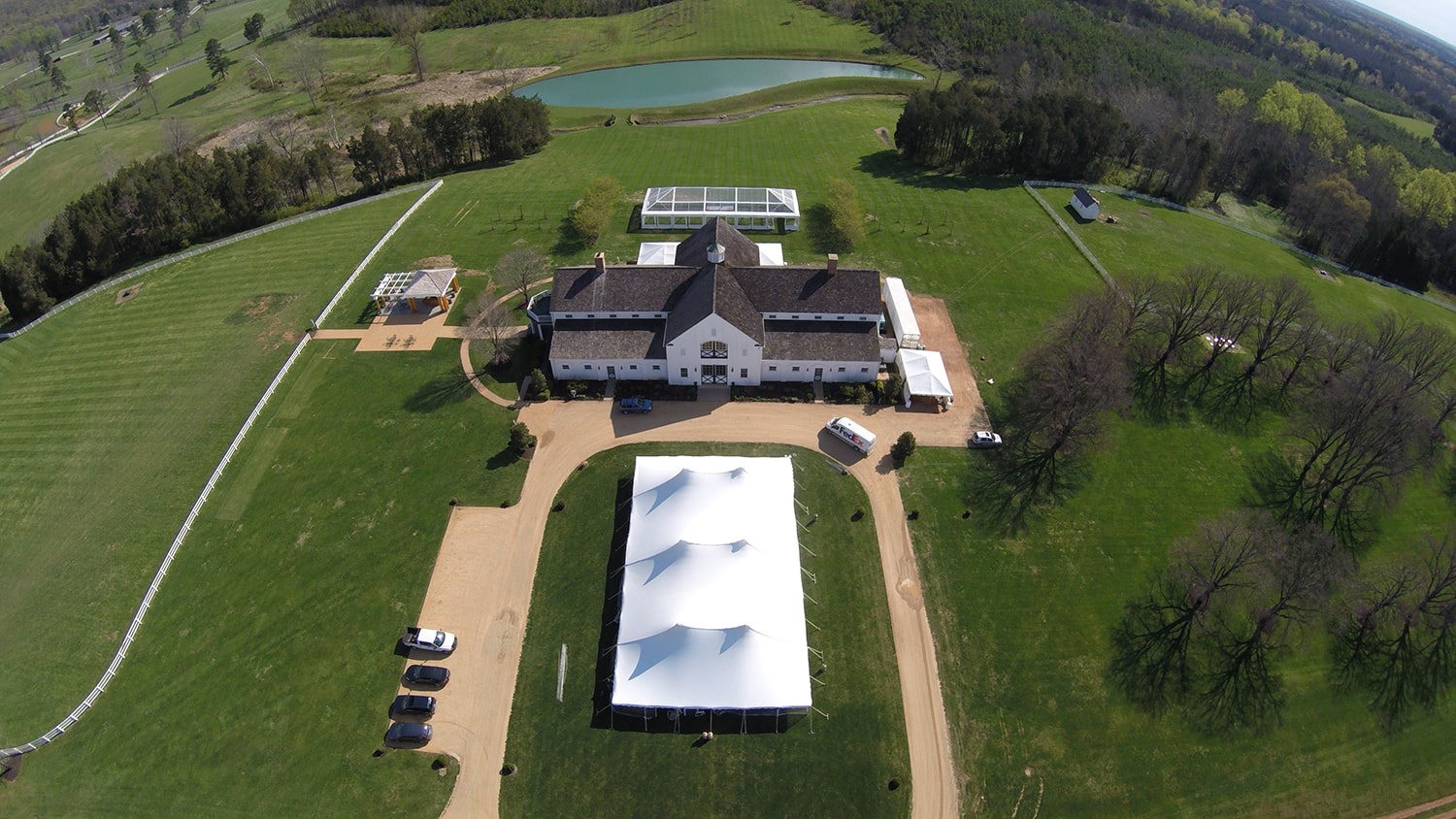 Overhead view of countryside venue featuring sailcloth tent beside main building and pond.